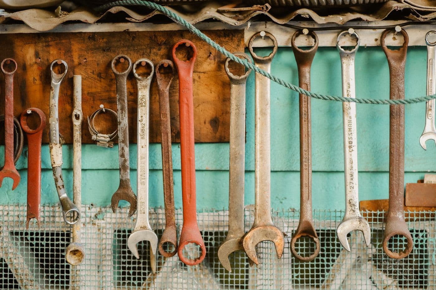 A row of well-used combination and open-ended wrenches hanging in size order on a workshop wall above a green painted bench.